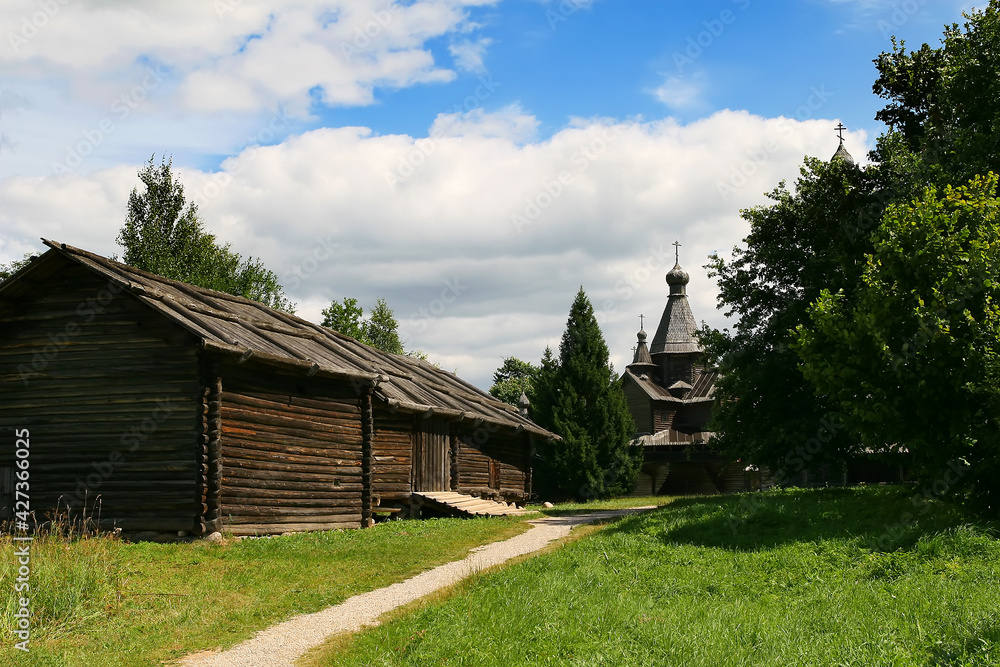 Old log buildings. On the left is a wooden warehouse. In the center there is a path leading into the distance to an old wooden church. Old log buildings. On the left is a wooden warehouse. In the center there is a path leading into the distance to an old wooden church.