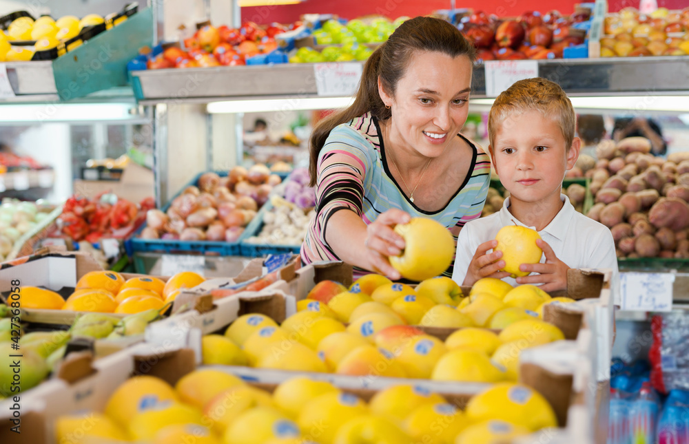 Happy cheerful smiling mother with little boy buying pears and apples at store