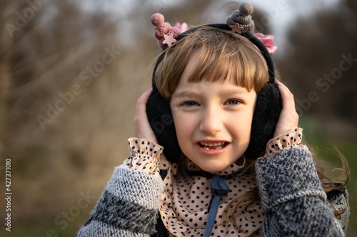 A portrait of a seven-year-old girl in soft warm headphones  in a dress with polka dots and in an autumn coat  listening to music on the street.