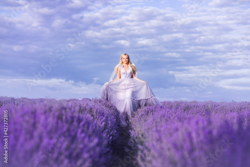 beautiful woman in a lush long dress runs in a lavender field. A girl in the image of a fairy and a princess of flowers.