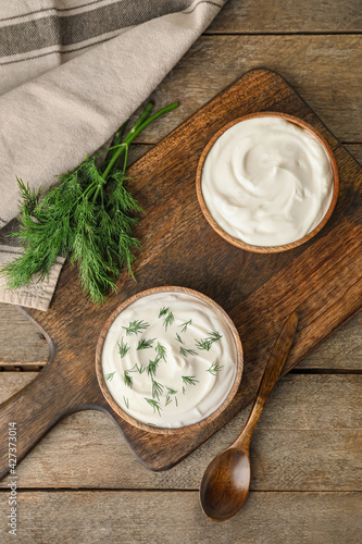 Bowls of tasty sour cream on wooden background