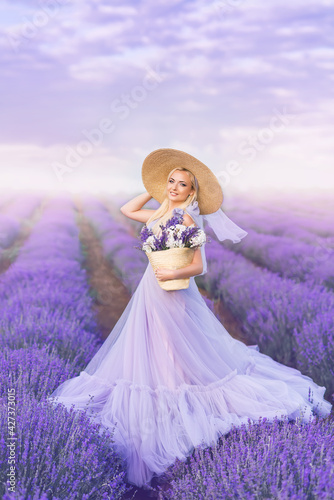 beautiful woman in a long purple dress and a large hat in lavender. A girl with a basket of flowers in a lavender field.