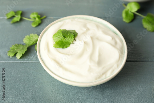 Bowl of tasty sour cream and herbs on color wooden background