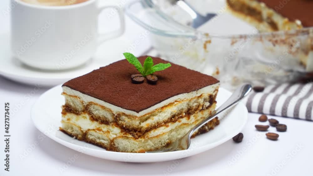 Traditional Italian Tiramisu dessert in glass baking dish, portion on plate and cup of coffee Traditional Italian Tiramisu dessert in glass baking dish, portion on plate and cup of coffee