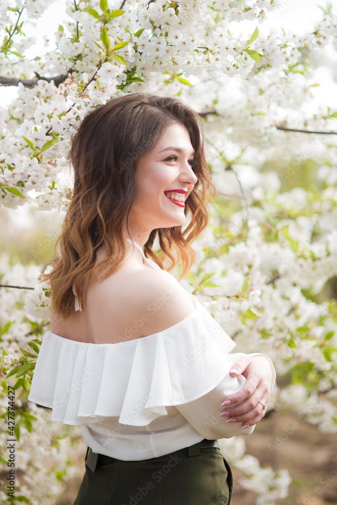 Lovely young girl in a white romantic silk blouse in spring in a blooming cherry garden in sunny weather. Spring and Fashion. Spring blooming gardens Lovely young girl in a white romantic silk blouse in spring in a blooming cherry garden in sunny weather. Spring and Fashion. Spring blooming gardens