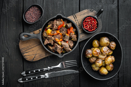 Beef meat and vegetables stew, in cast iron frying pan, on black wooden background, top view flat lay
