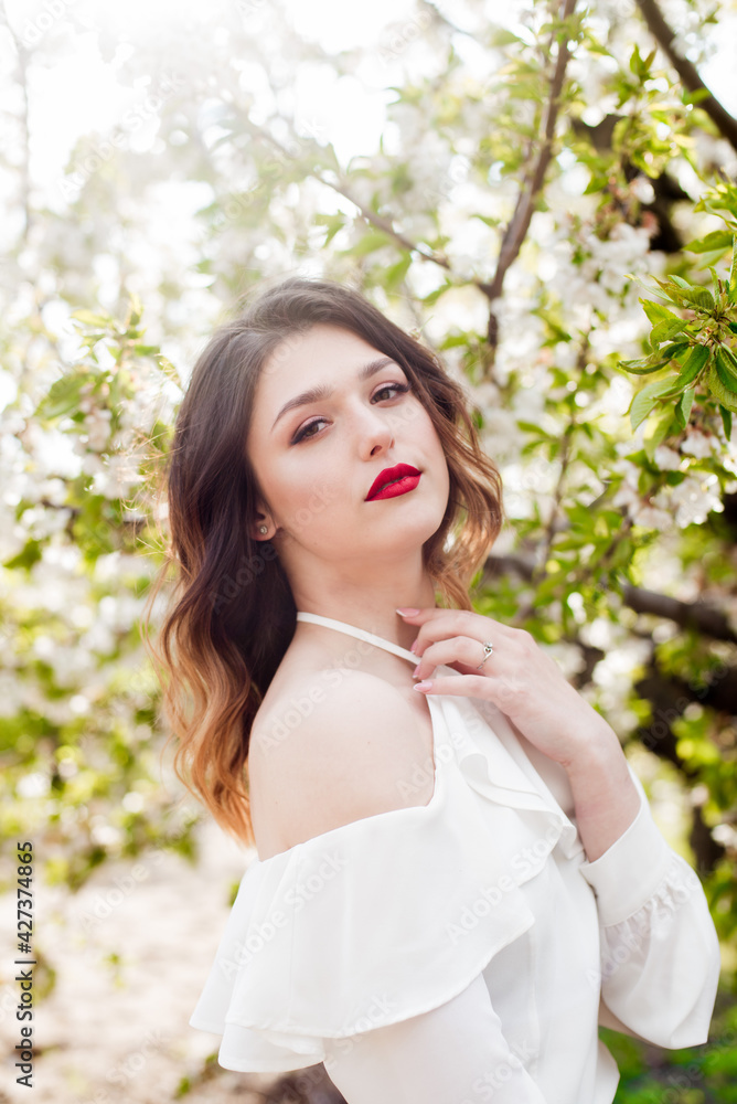 Lovely young girl in a white romantic silk blouse in spring in a blooming cherry garden in sunny weather. Spring and Fashion. Spring blooming gardens Lovely young girl in a white romantic silk blouse in spring in a blooming cherry garden in sunny weather. Spring and Fashion. Spring blooming gardens