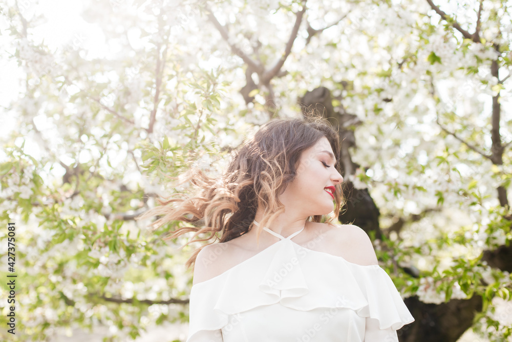 Lovely young girl in a white romantic silk blouse in spring in a blooming cherry garden in sunny weather. Spring and Fashion. Spring blooming gardens Lovely young girl in a white romantic silk blouse in spring in a blooming cherry garden in sunny weather. Spring and Fashion. Spring blooming gardens