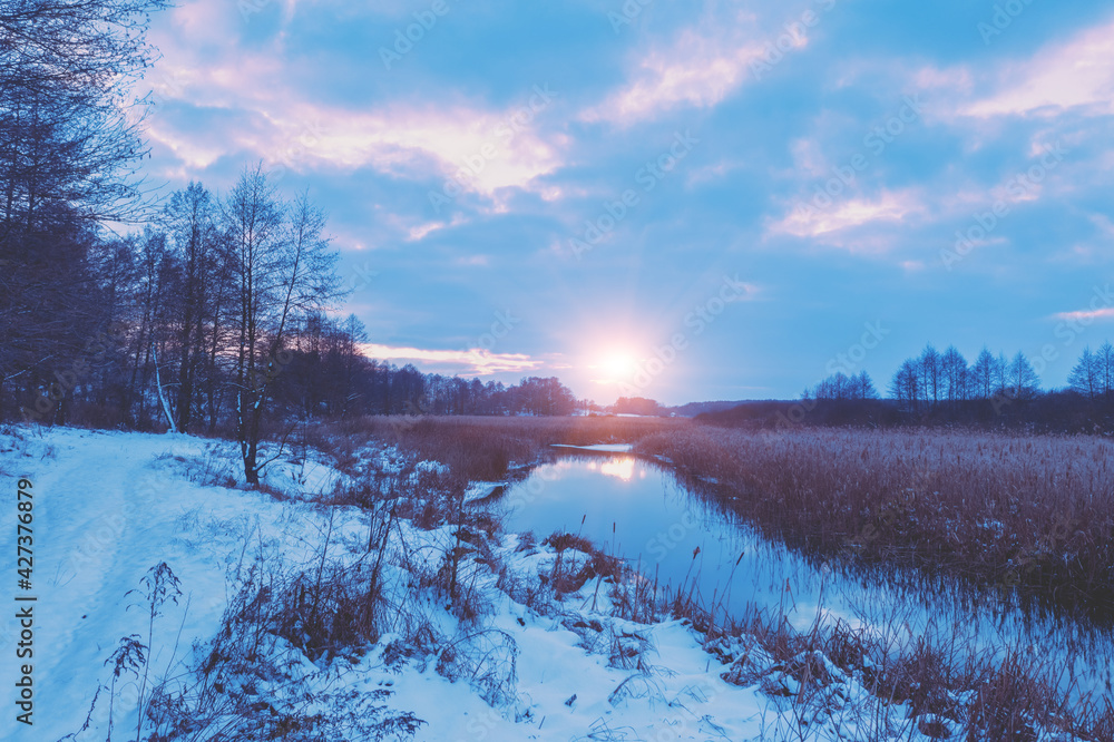 Rural landscape in winter. View of the brook and cloudy sky at sunset.