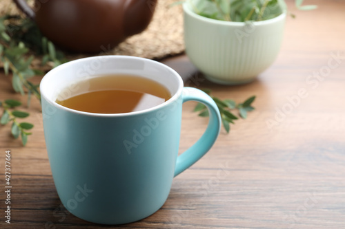 Cup of aromatic eucalyptus tea on wooden table, closeup. Space for text