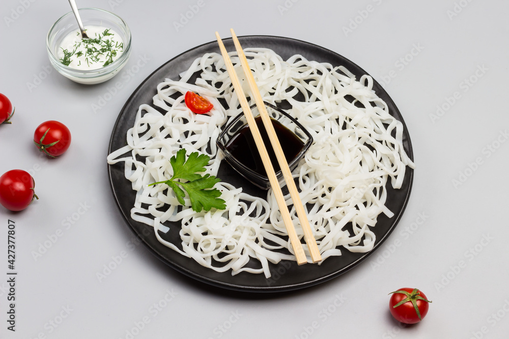 Rice noodles with sauce, bamboo sticks on black plate. Cherry tomatoes in bowl with white sauce on table Rice noodles with sauce, bamboo sticks on black plate. Cherry tomatoes in bowl with white sauce on table