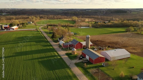 Establishing shot of American midwestern countryside in springtime. Aerial view of farms with red barns in spring, rural road, agricultural fields. Camera moves forward and pans to the left