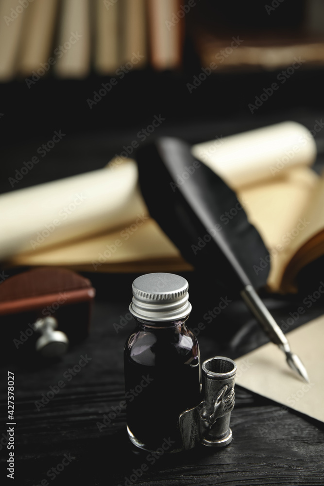 Feather pen and bottle of ink on black wooden table