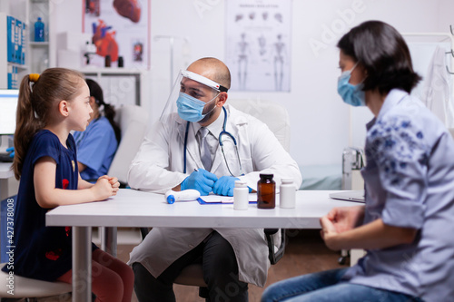 Medical doctor wearing face mask and visor writing prescription on clipboard against covid19. Practitioner specialist in medicine providing professional treatment services in hospital clinic.
