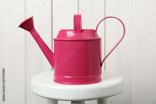 Pink metal watering can on table against white wooden background