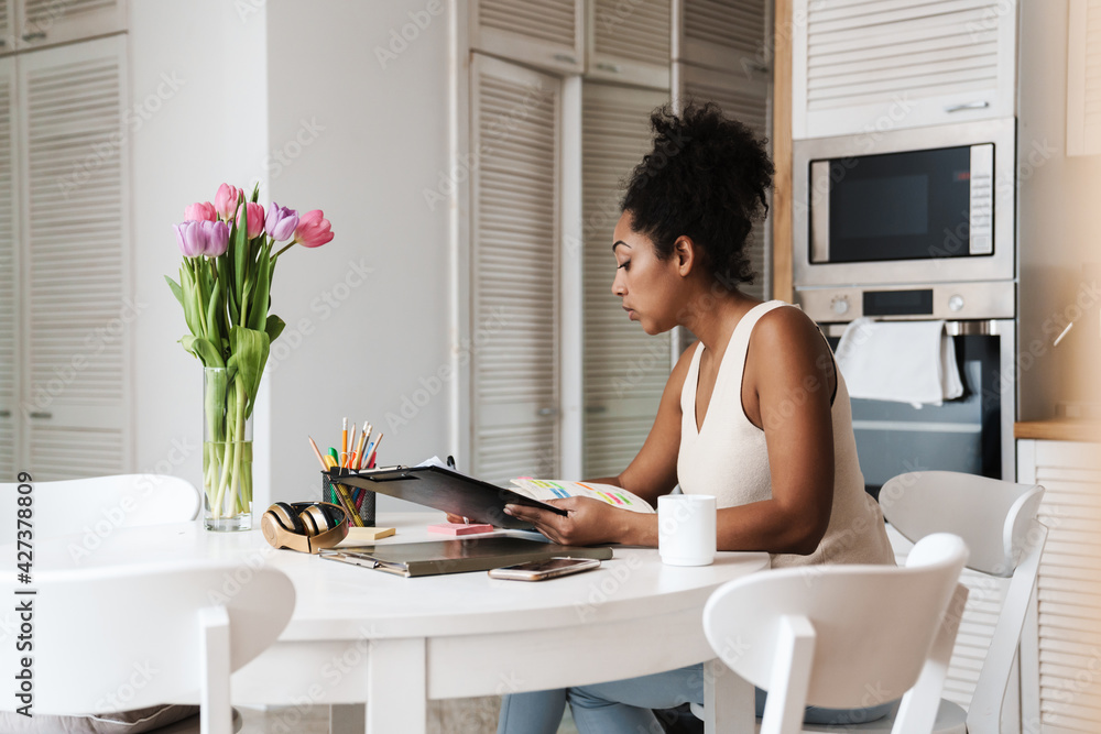 Black woman working with papers while sitting at table in home kitchen Black woman working with papers while sitting at table in home kitchen