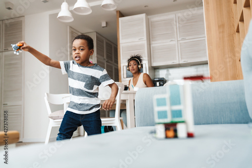 Black boy in t-shirt running and playing with toy at home