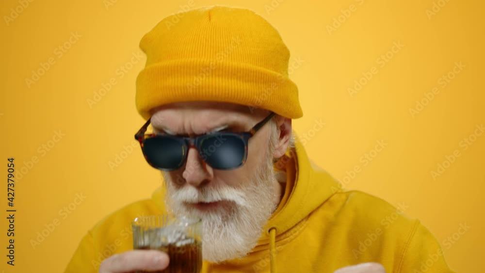 Cheerful elderly man relaxing indoors. Old guy drinking alcohol in studio. Cheerful elderly man relaxing indoors. Old guy drinking alcohol in studio.