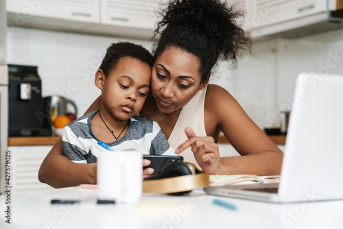 Black mother and son using mobile phone while sitting together at home © Drobot Dean