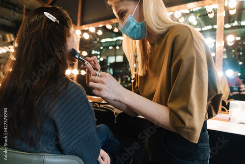 Blonde woman in face mask doing makeup for her client in beauty salon