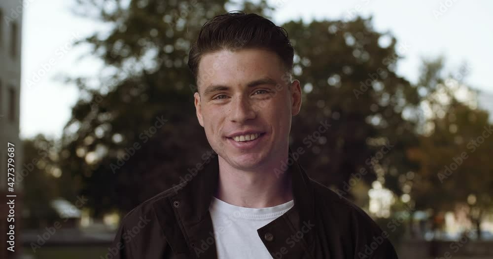 Close-up young man wears casual clothes stands posing outdoors talking to camera active friendly talks. Head shot caucasian guy teen student at city street communicates conducting dialogue alone Close-up young man wears casual clothes stands posing outdoors talking to camera active friendly talks. Head shot caucasian guy teen student at city street communicates conducting dialogue alone