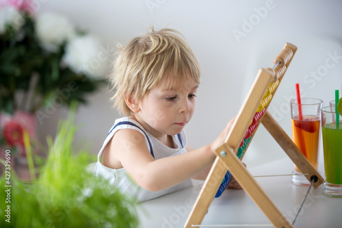 Sweet toddler child, blond boy, learning math at home with colorful abacus