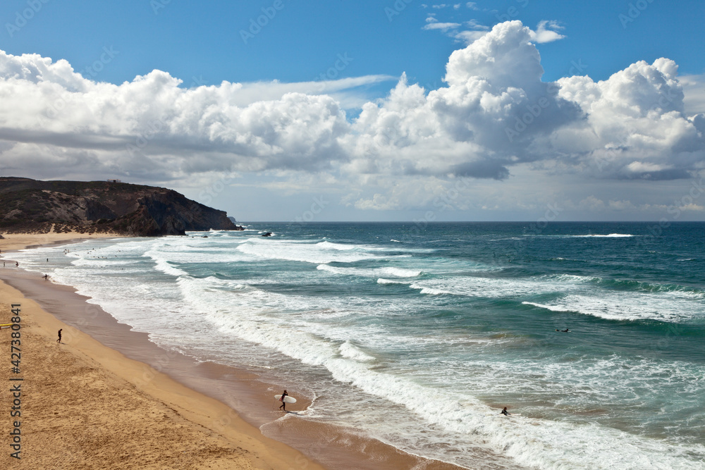 Tourists and outdoor enthusiasts come to Portuguese coast of the Atlantic Ocean to the beautiful sandy beach of Praia do Amado in Algarve to surf the ocean waves. Active holidays. Picturesque seascape