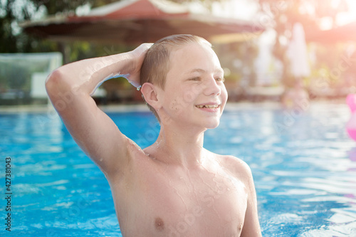 Close-up portrait of happy teen boy in the swimming pool at aquapark. Cute child having fun enjoyable time on vacation. Looking at camera.