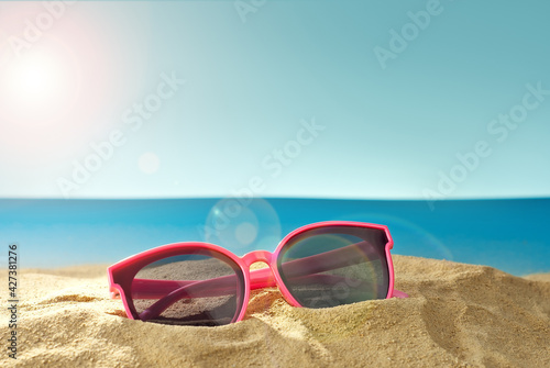 Pink glasses on the sand close up. Glasses on the beach on a background of blue water and sky. Summer, sea and vacation concept.