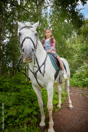 A teenage girl and a horse in nature among green trees © keleny