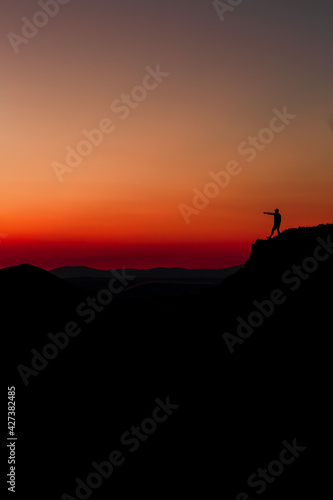 Red sunset with mountain silhouette. A man on mountain in sunset. Traveler on rock waving hands.