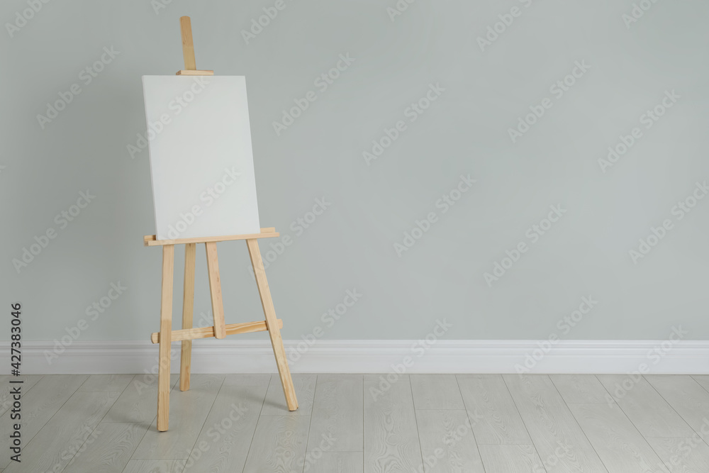 Wooden easel with blank canvas near light wall. Space for text Wooden easel with blank canvas near light wall. Space for text