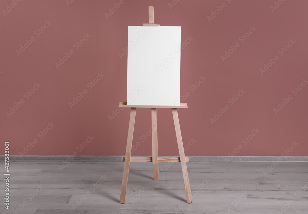Wooden easel with blank canvas near dusty rose wall Wooden easel with blank canvas near dusty rose wall