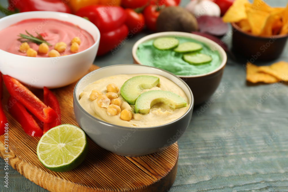 Different kinds of tasty hummus with ingredients on light blue wooden table Different kinds of tasty hummus with ingredients on light blue wooden table