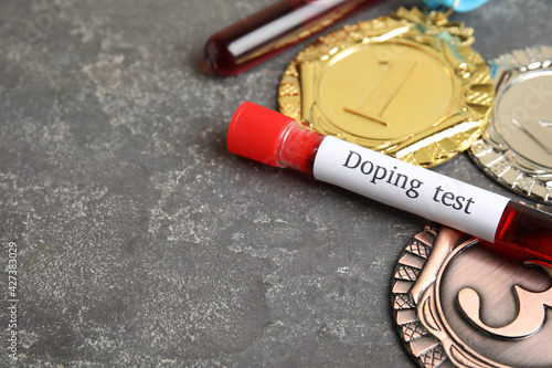 Medals and tube of blood with words Doping test on grey stone table. Space for text photo