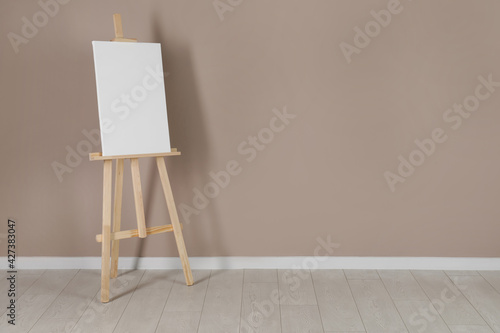 Fototapeta Naklejka Na Ścianę i Meble -  Wooden easel with blank canvas near beige wall. Space for text