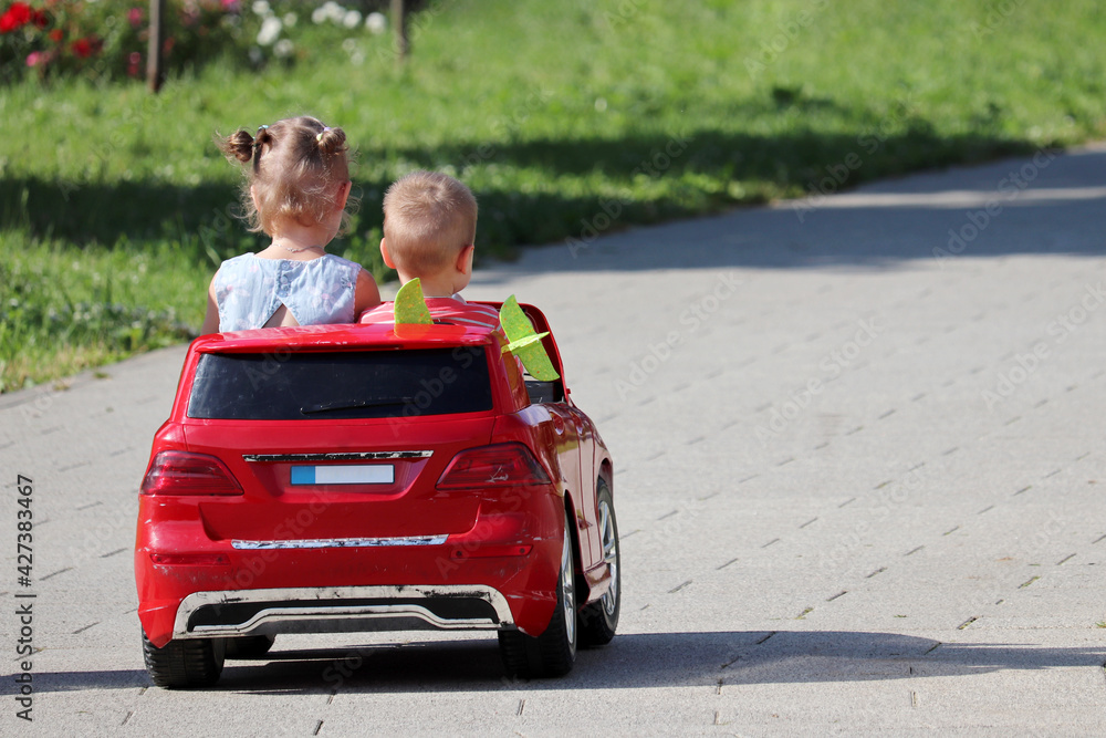 Little girl and boy riding a toy car in a park. Couple of kids having fun, children leisure, driving training Little girl and boy riding a toy car in a park. Couple of kids having fun, children leisure, driving training
