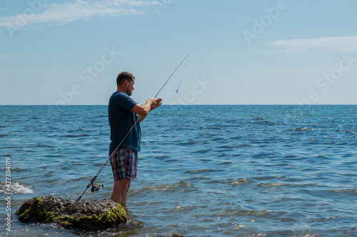 man with fishing rod. stands on the ankle in sea water on the stones