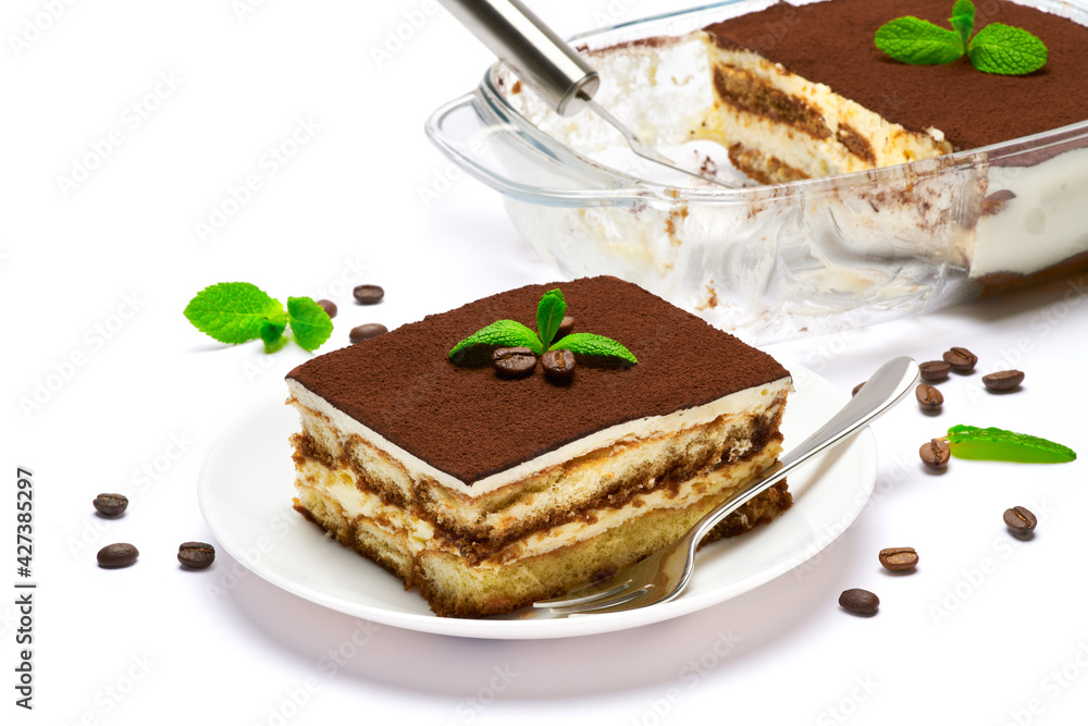 Traditional Italian Tiramisu dessert in glass baking dish, portion on plate and scapula isolated on white background Traditional Italian Tiramisu dessert in glass baking dish, portion on plate and scapula isolated on white background
