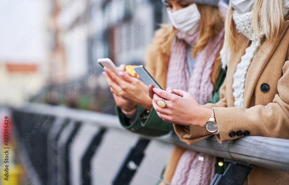 Two women using smartphones and wearing masks in the city