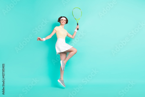 Full length body size view of lovely sportive cheerful girl jumping playing tennis isolated over bright teal turquoise color background © deagreez