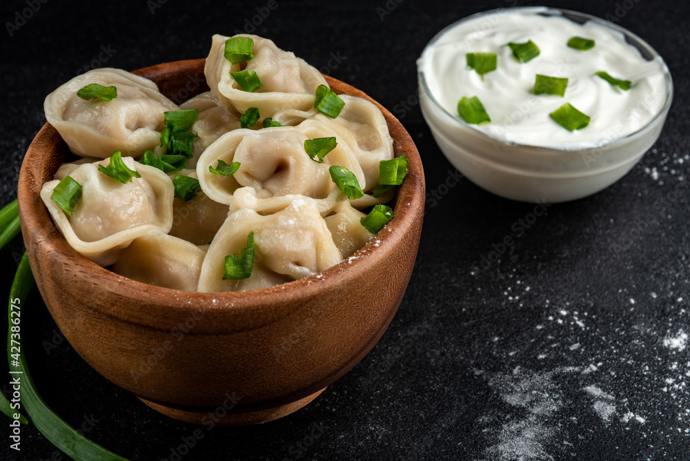 Meat dumplings in wooden bowl with sour cream and green onion on black background. Meat dumplings in wooden bowl with sour cream and green onion on black background.
