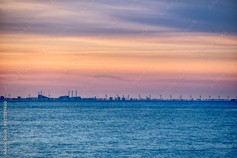 Copenhagen skyline at sunset with turbines rotating away in the Danish wind farm. Baltic Sea wind power plant with the city 's industrial skyline raises concerns about pollution and sustainable energy