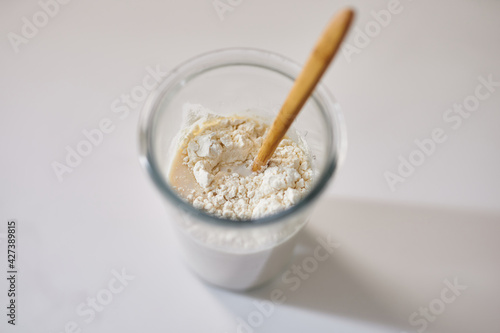 Mixing yeast dough starter ingredients concept: milk, sugar, fresh wild yeast and flour all together in transparent glass on white table. High quality top view photo