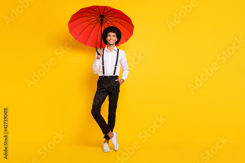 Full length photo portrait of african american guy posing with red umbrella isolated on vivid yellow colored background