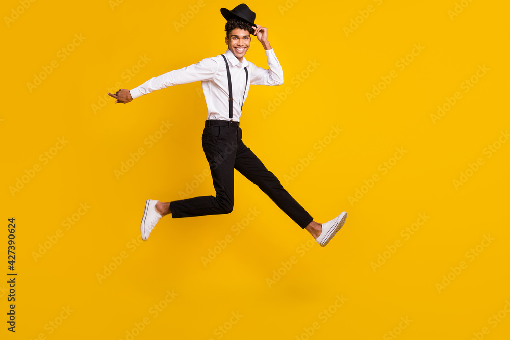 Full length photo portrait of african american man running taking off hat jumping up isolated on vivid yellow colored background Full length photo portrait of african american man running taking off hat jumping up isolated on vivid yellow colored background