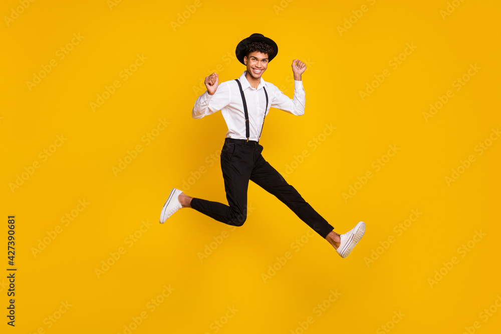 Photo of funky crazy guy jump raise fists wear headwear shirt suspenders sneakers isolated yellow color background