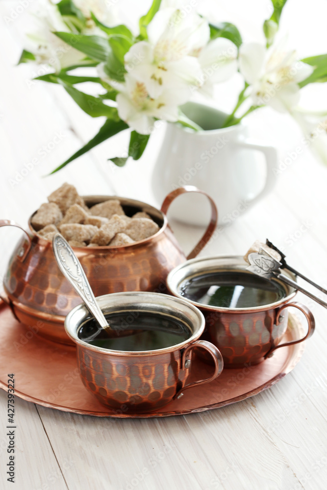 Fototapeta premium Still life with coffee, brown sugar in a copper bowl and white alstroemeria flowers. Morning coffee. Authentic copper tableware. Vertical frame.