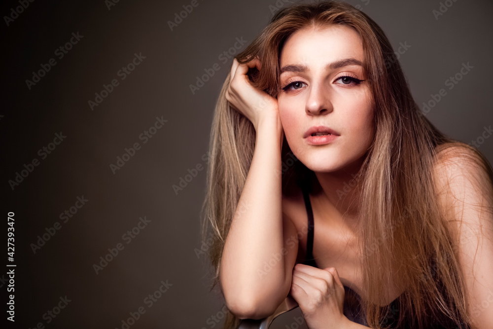 Natural Sensual Portrait of Charming Caucasian Blond Girl With Long Beautiful Hair Posing in Studio Against Dark Background. Natural Sensual Portrait of Charming Caucasian Blond Girl With Long Beautiful Hair Posing in Studio Against Dark Background.