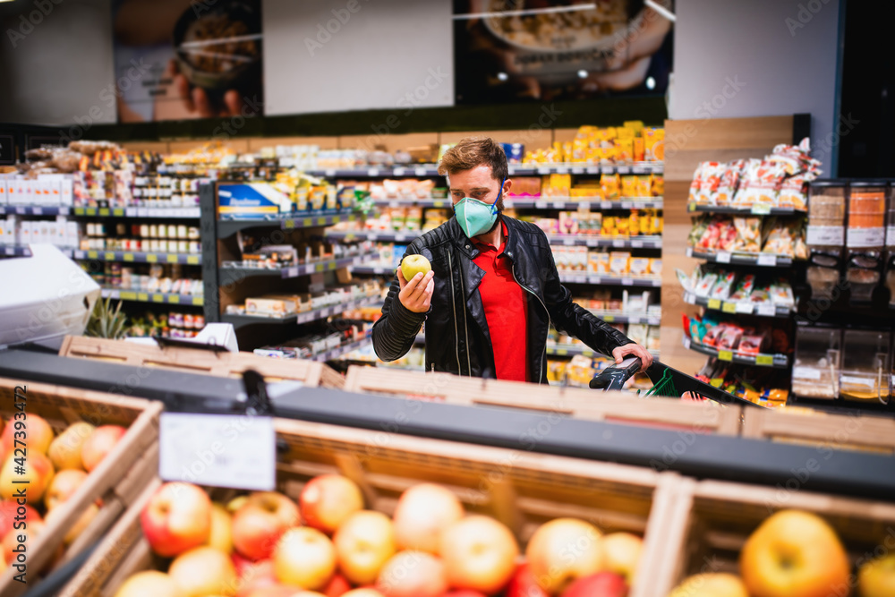 A Caucasian fit man with a face mask who buys healthy food at the supermarket. Procurement of food during the coronavirus pandemic COVID - 19